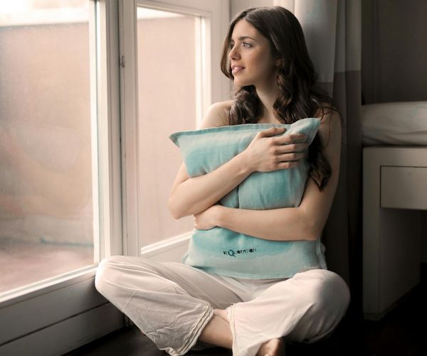 Smiling woman meditating in a bright, peaceful room with blue light accents.